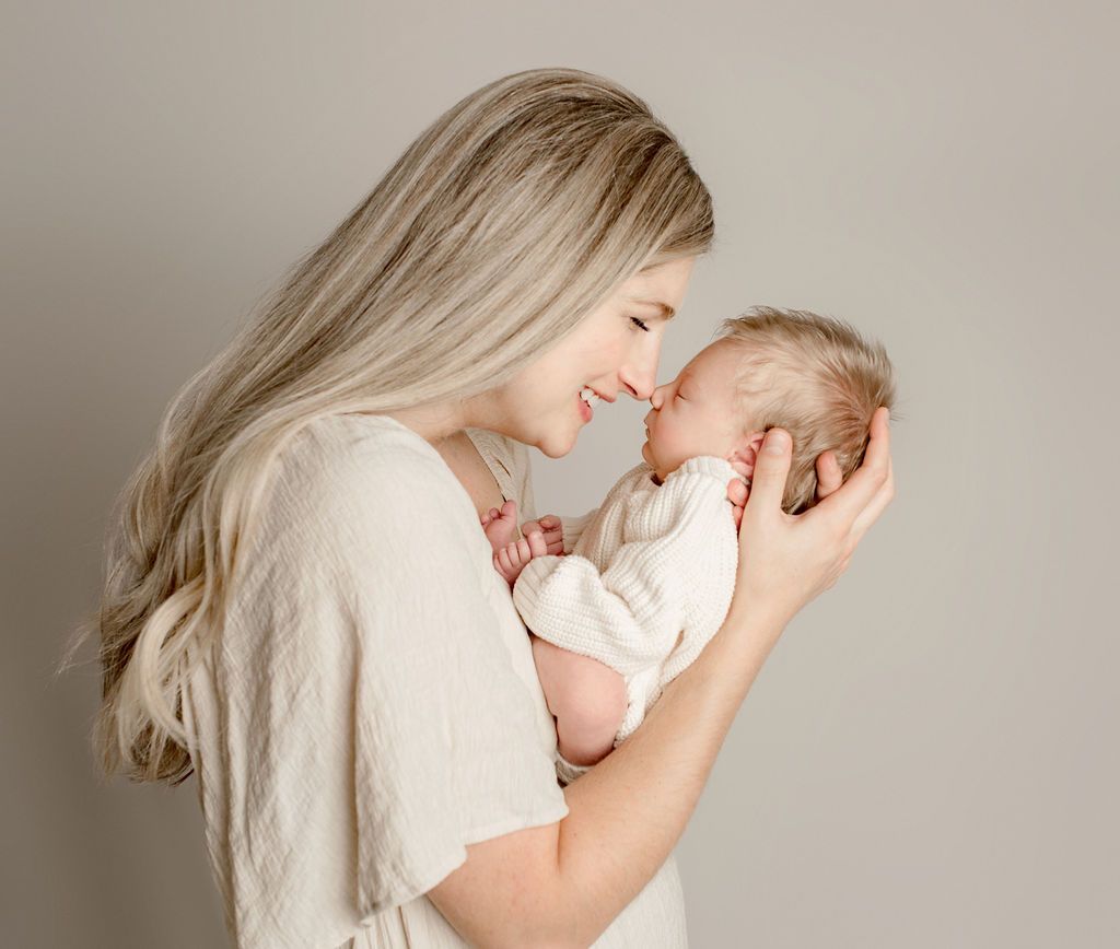 Mother and newborn touching noses, smiling; neutral background.