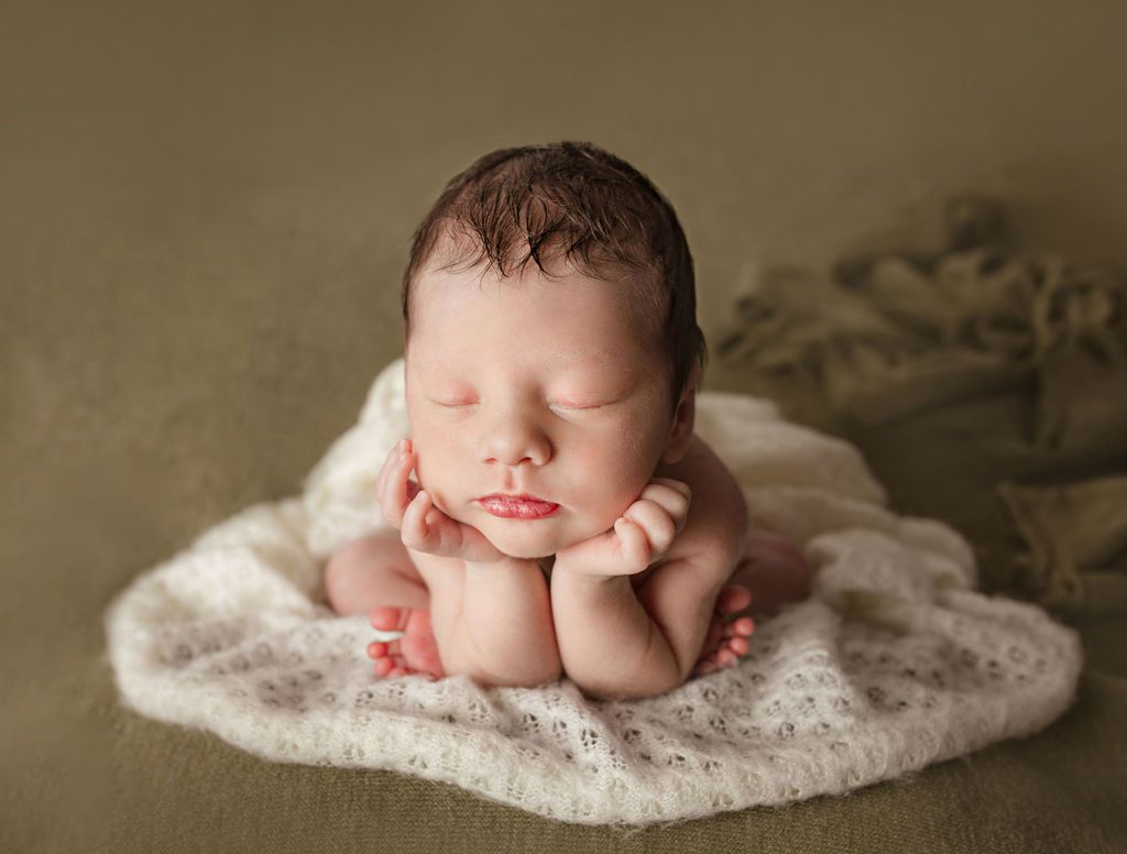 Newborn baby sleeping, curled on a white blanket, hands supporting head, green background.