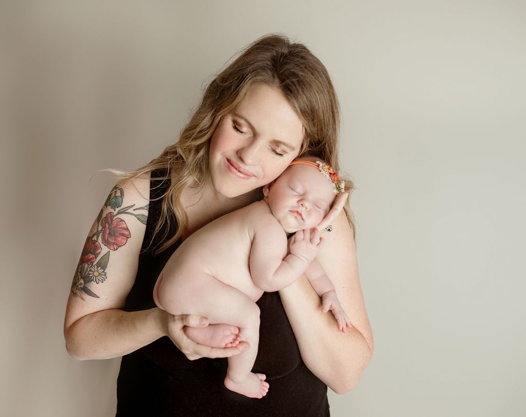 Woman holding a newborn baby. The woman is wearing a black tank top and has a tattoo on her arm. Both are smiling.