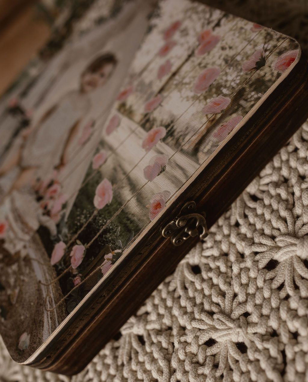 Wooden box with a photo of a couple amid pink flowers, resting on a textured white surface.