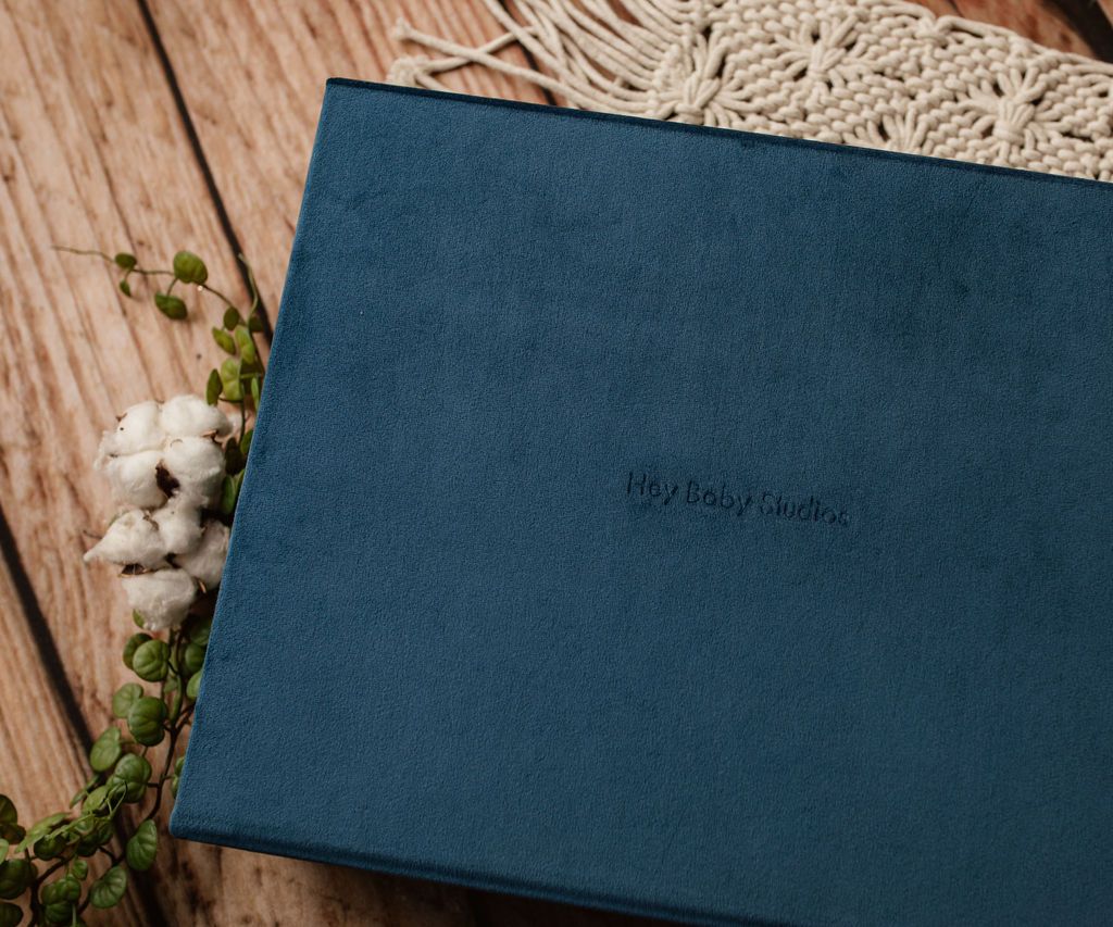 Blue velvet photo album with embossed text, on wooden surface with cotton and greenery.