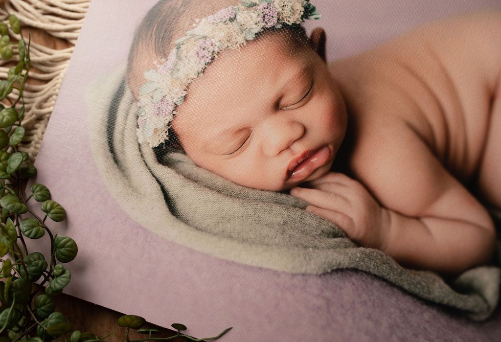 Newborn baby sleeping, wearing flower crown, on a pink blanket, near greenery.