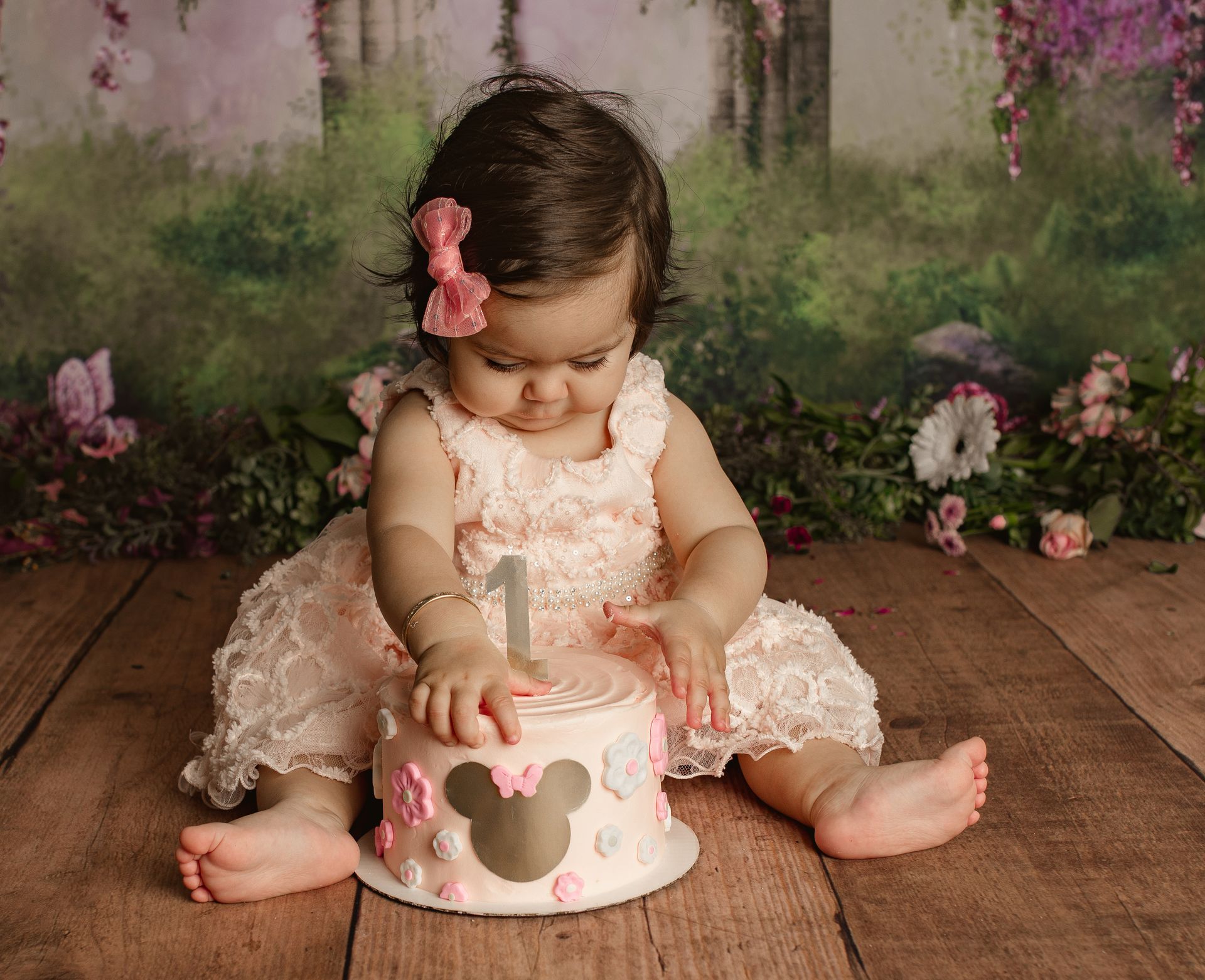 Toddler in pink dress, playing with a small decorated Minnie Mouse cake. First Birthday Session