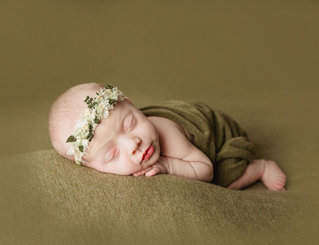 Sleeping infant with albinism wearing a floral headband, wrapped in green fabric, resting on a textured green blanket.