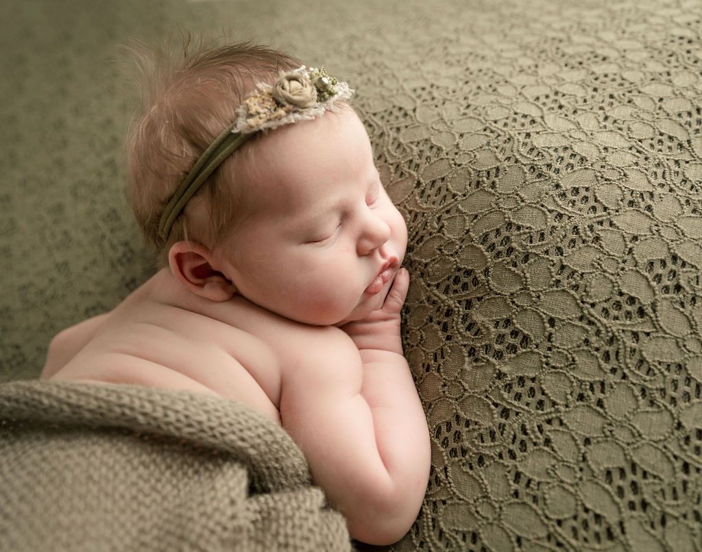 Sleeping baby with headband on a textured green blanket.