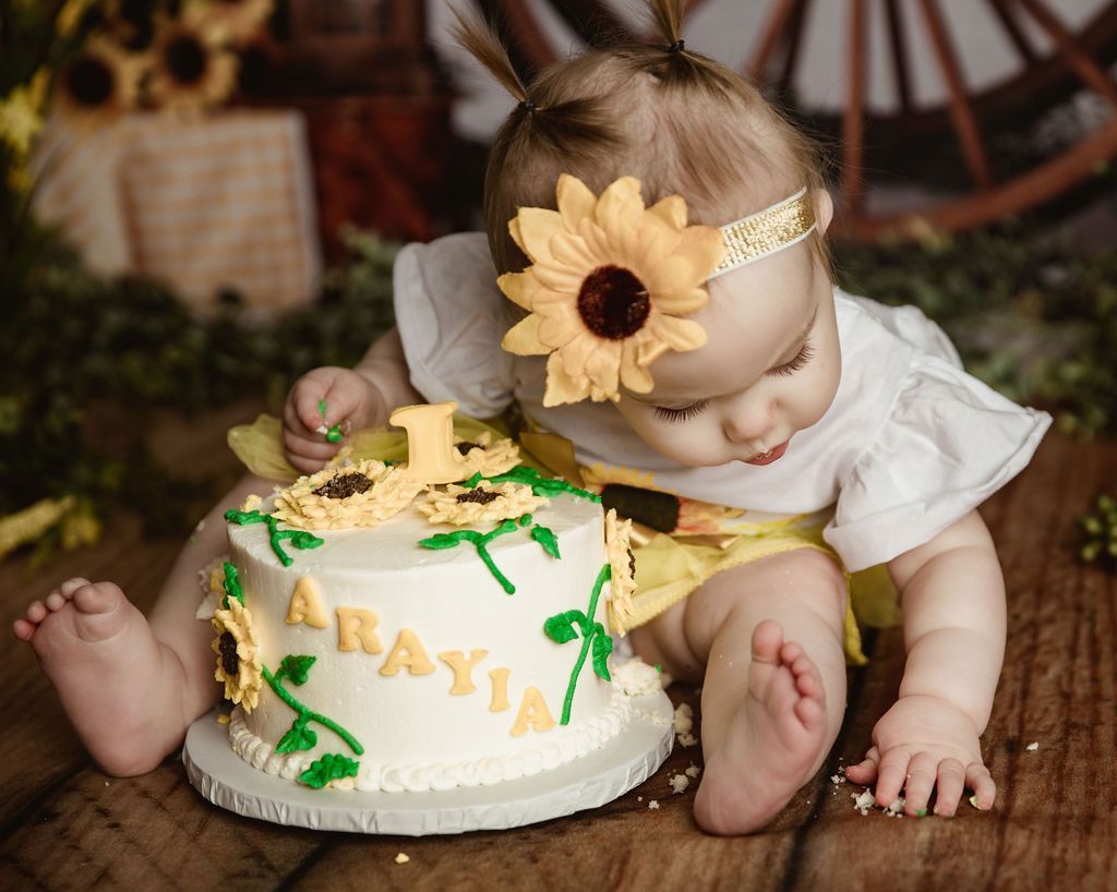 Baby with a sunflower headband and cake, celebrating a first birthday.