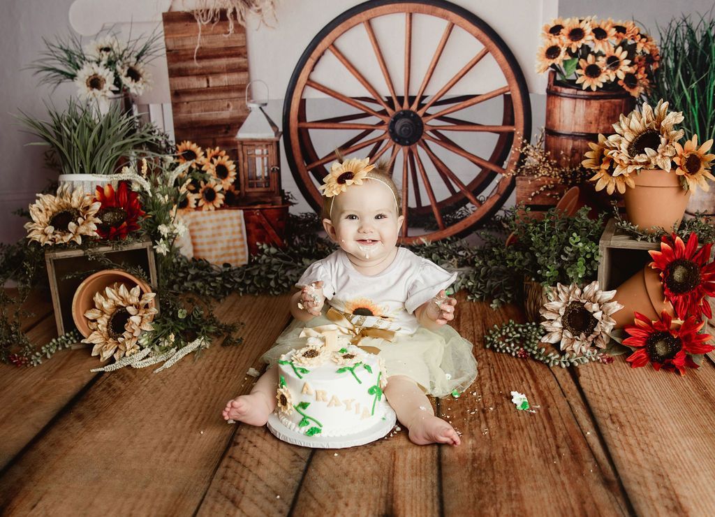 Child in sunflower-themed setting, smiling, covered in cake. 