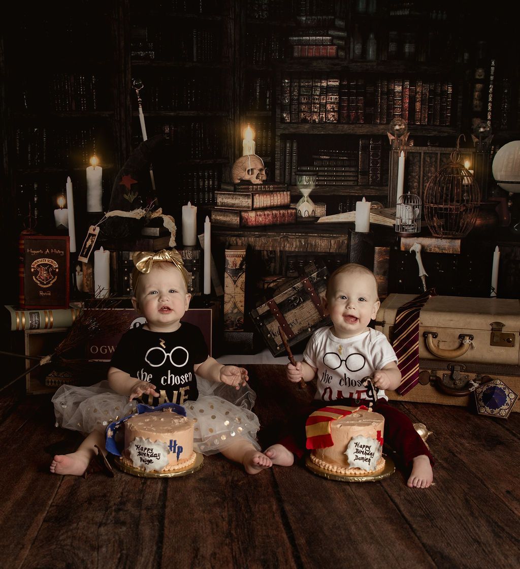 Twins in Harry Potter themed outfits sitting by cakes in front of a bookcase.