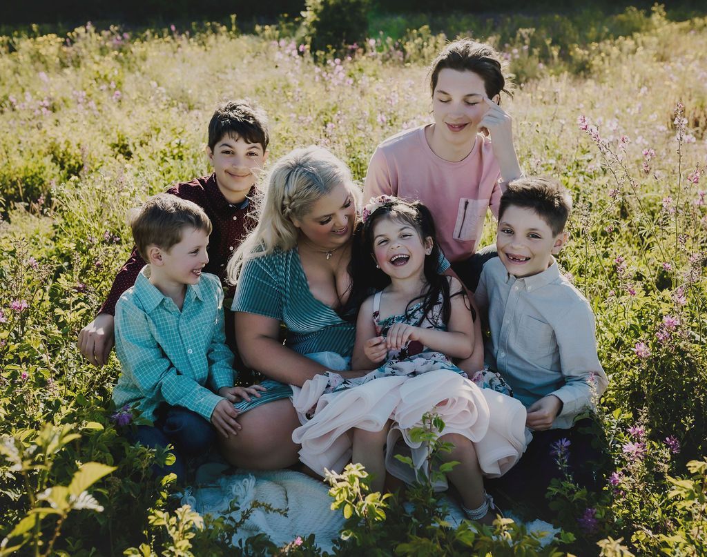 Woman smiles surrounded by five children in a field of flowers. All are smiling; two are laughing.