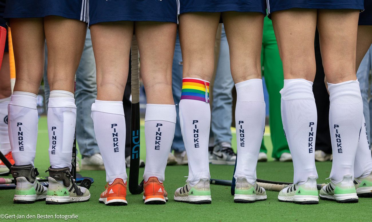 Voetballers staan in een rij op een grasveld, met witte sokken en kleurrijke voetbalschoenen aan.
