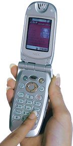 Een zilverkleurige klaptelefoon ligt open in een hand, met een duim die op het toetsenbord drukt.