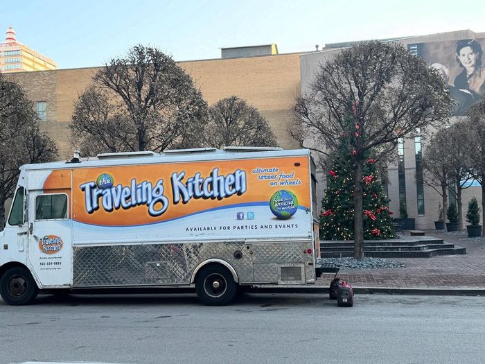 A traveling kitchen food truck is parked on the side of the road