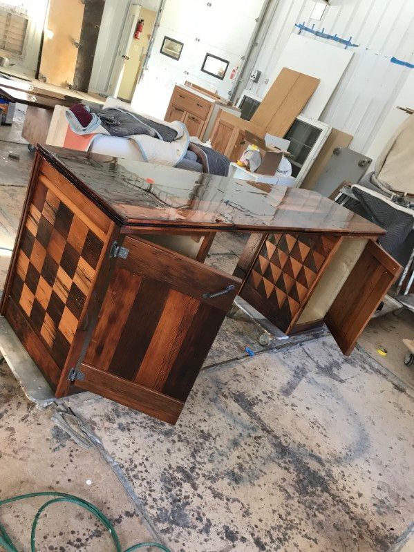 Wooden desk with checkerboard-patterned sides and dark, glossy finish in a workshop setting.