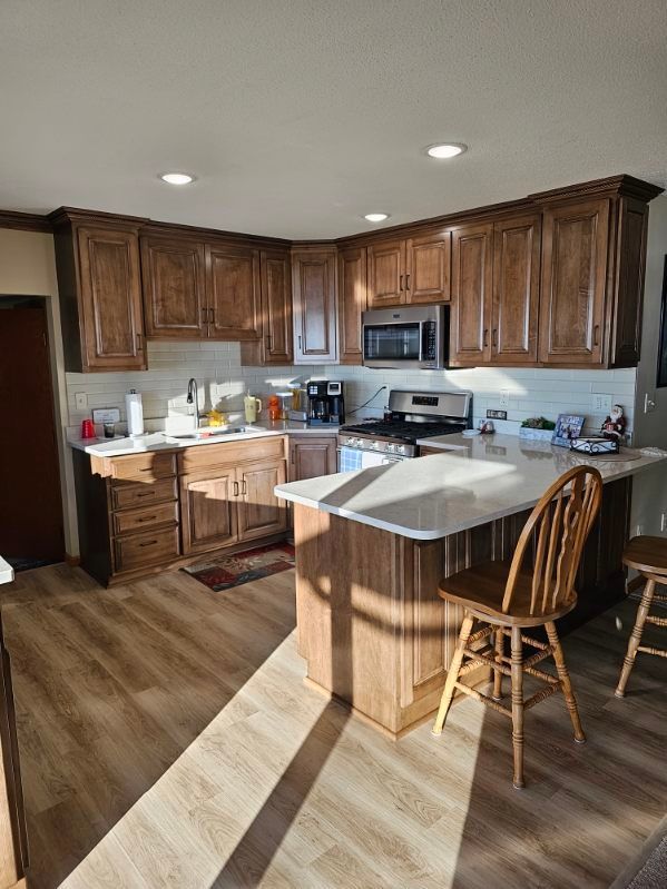 Kitchen with brown cabinets, white countertops, and wood-look flooring. Sunlight streams in.