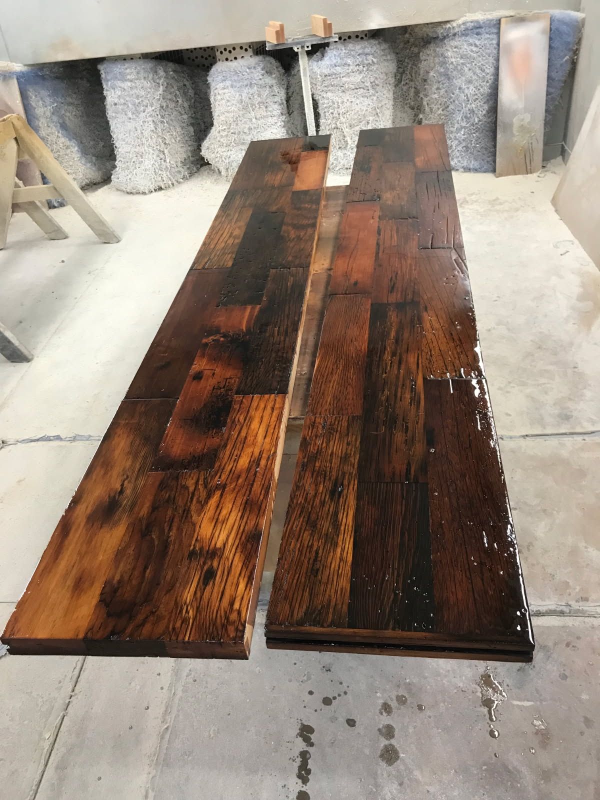Two stained wooden planks on a concrete floor. The wood has a dark, glossy finish.