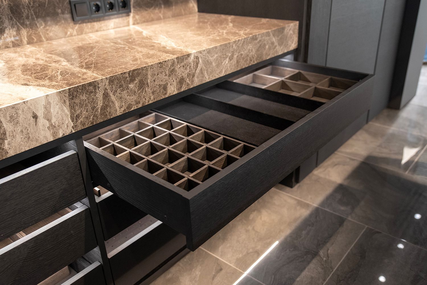 Black kitchen drawer open, revealing storage compartments against a marbled countertop.