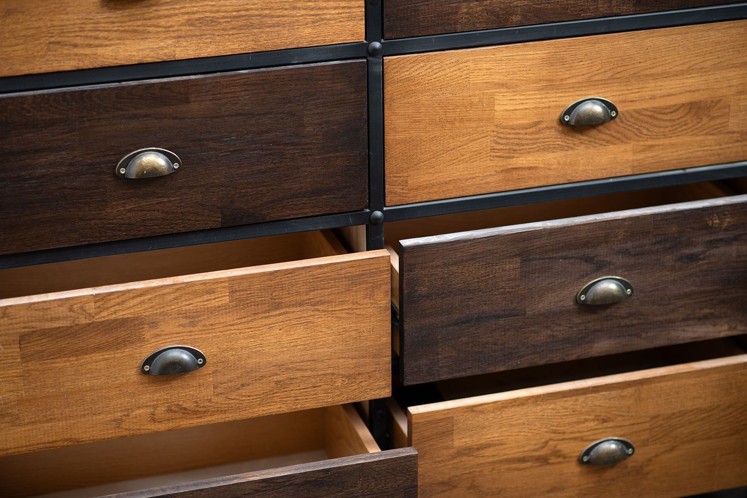 Wooden dresser with various open and closed drawers, featuring bronze handles and a two-tone wood stain.