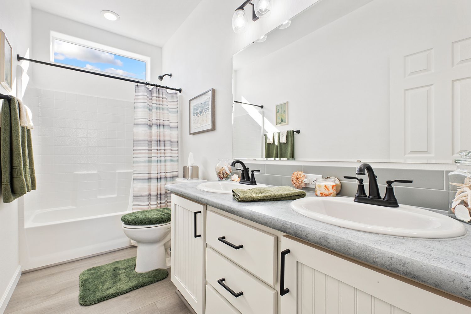 Bathroom with white vanity, double sinks, bathtub, toilet, green accents, and a window.