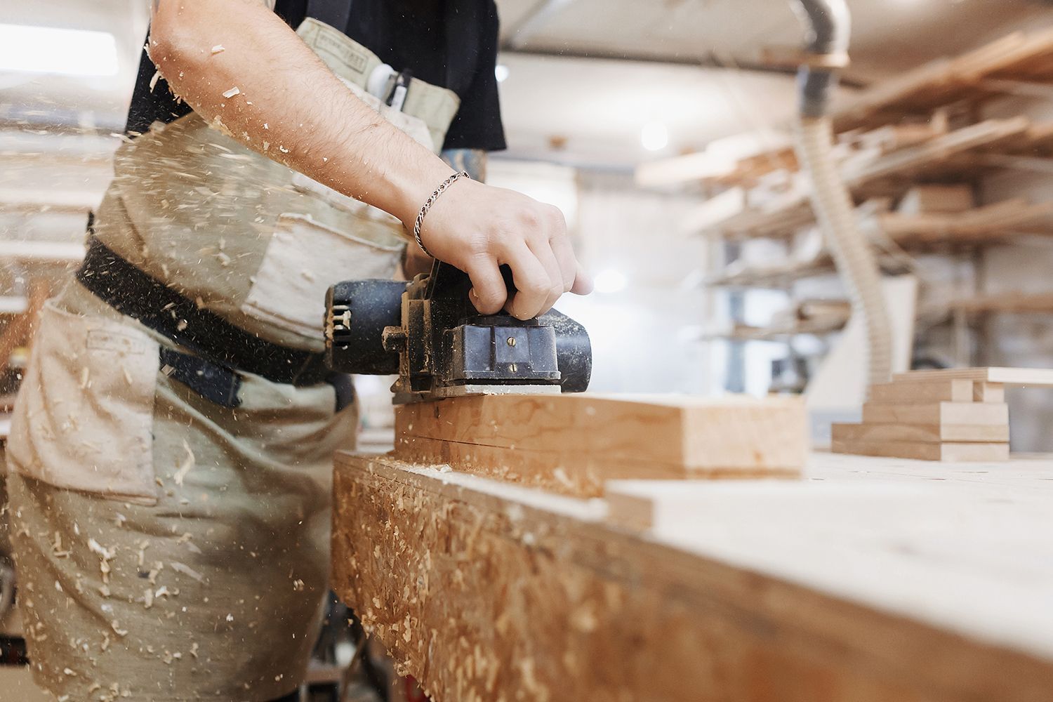 Carpenter using a planer on wood in a workshop, sawdust flying.