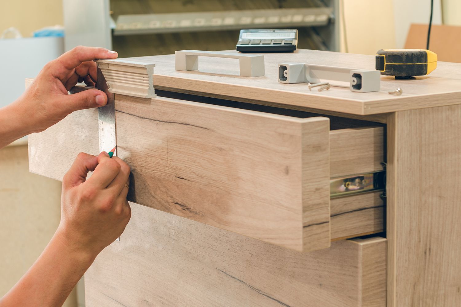 Person installing drawer front on a light wood cabinet with silver hardware.