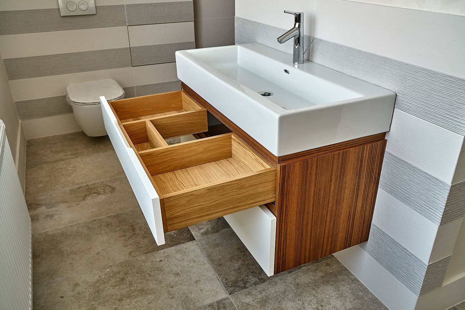 Bathroom vanity with open drawer; white sink and drawer front, wood cabinet, gray and white tile.