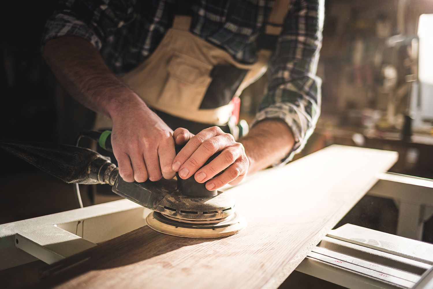 Person using a sander on a wooden plank in a workshop.