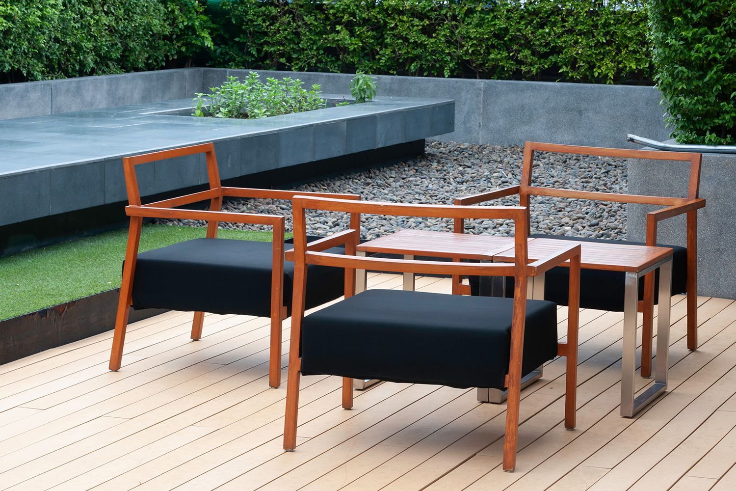 Three modern wooden chairs with black seats and two small tables on a wooden deck.