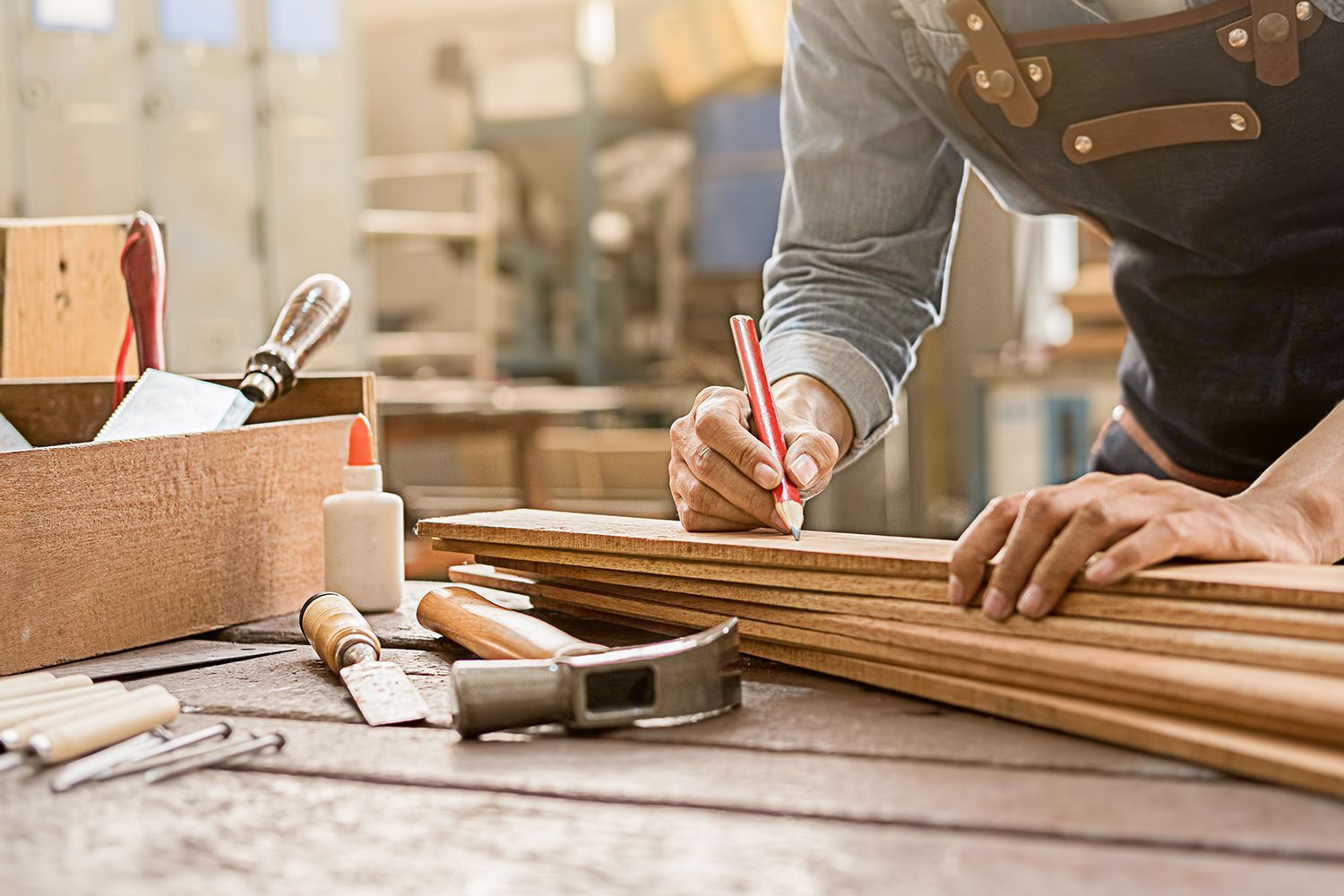 Carpenter marking wood planks with a pencil at a workbench in a workshop.