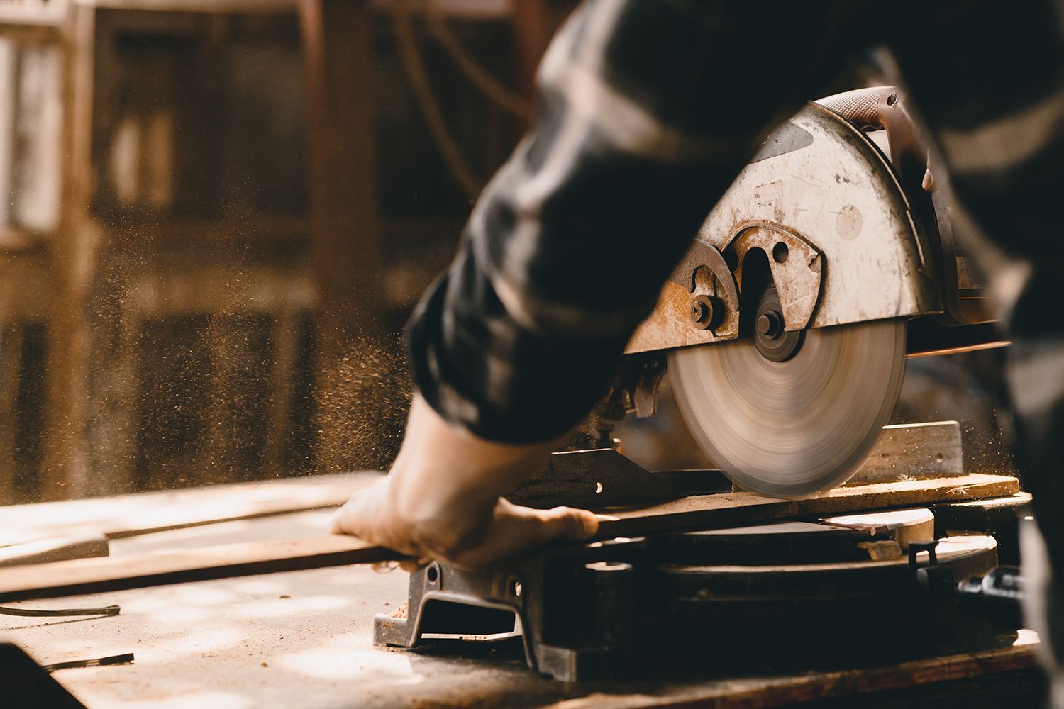 A person using a circular saw to cut wood in a workshop, sawdust in the air.