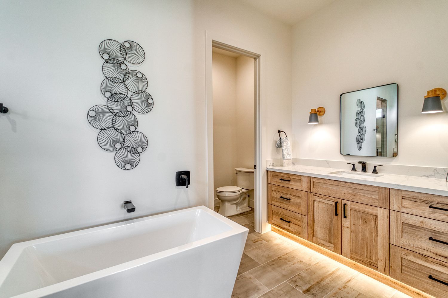 Modern bathroom with white tub, light wood vanity, and decorative wall art.