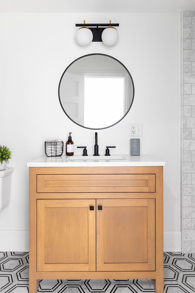 Bathroom vanity with round mirror, globe lights, and wood cabinet. Black and white patterned floor.