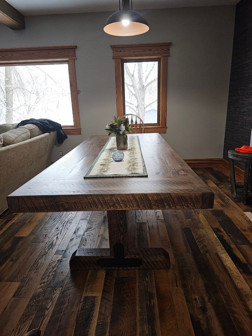 Rustic wooden dining table with a center base and a floral centerpiece.