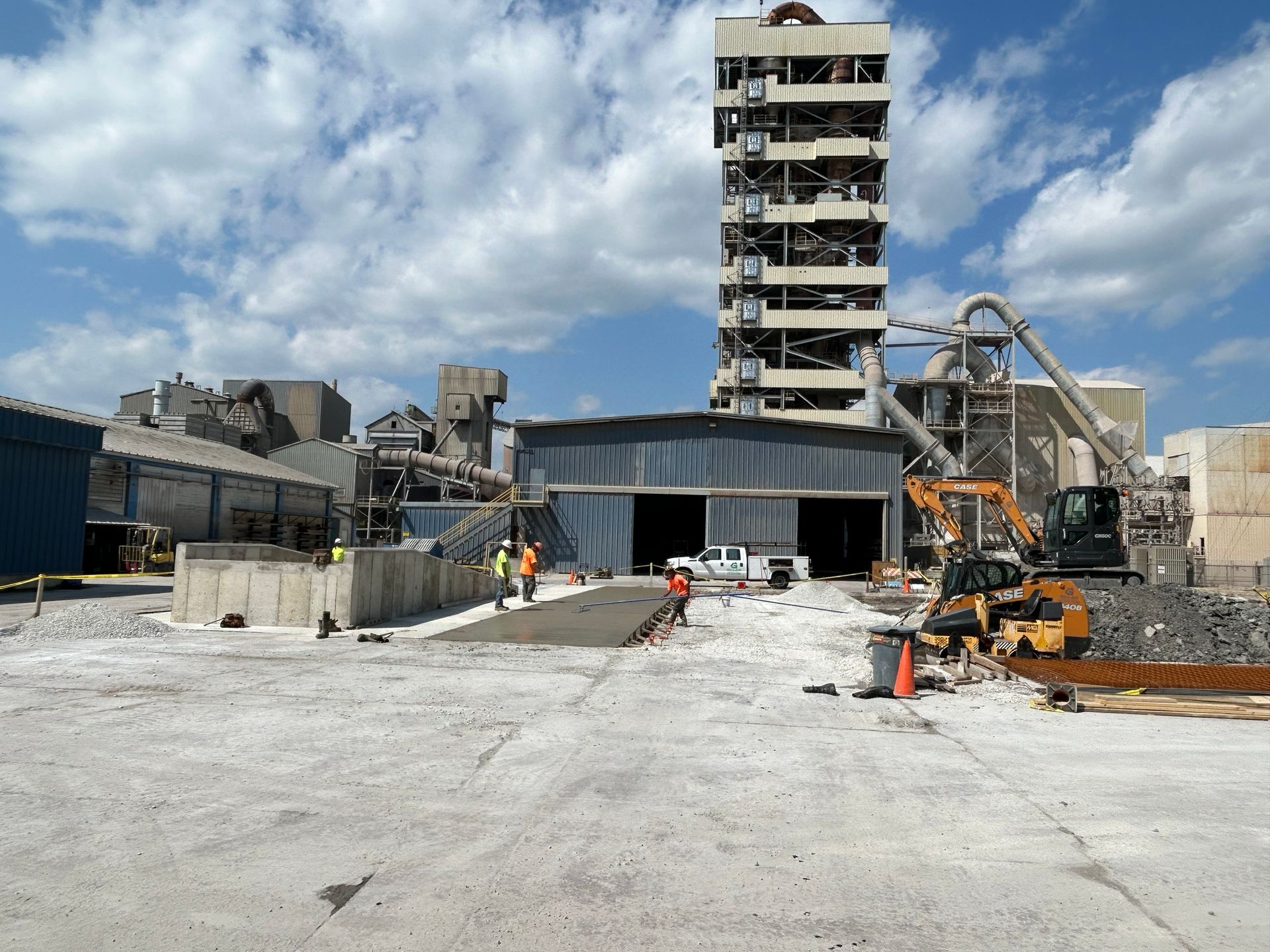 Demolished industrial buildings under a cloudy sky. Workers near heavy machinery.