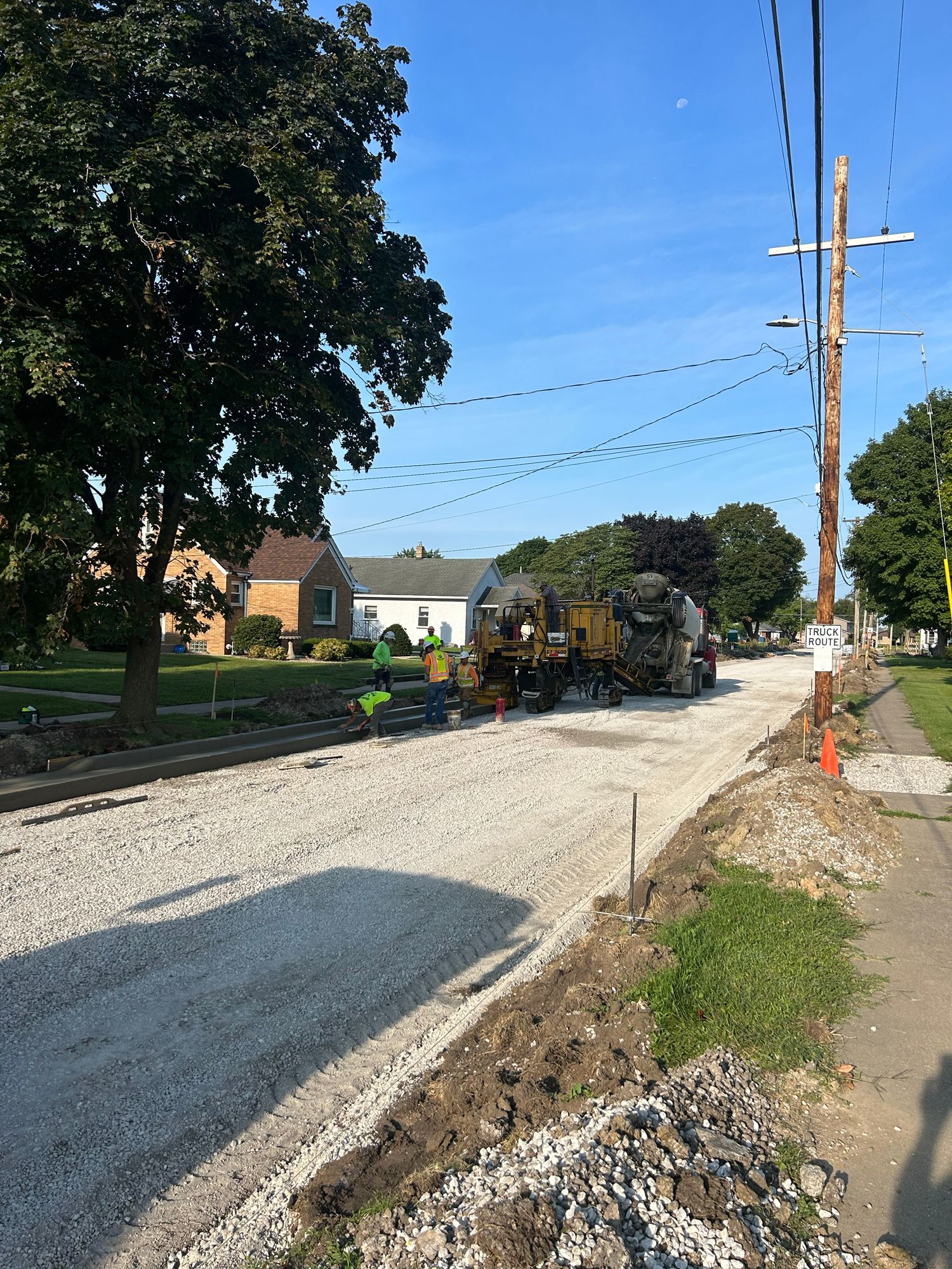 Street construction site with gravel, a cement truck, and utility poles on a sunny day.
