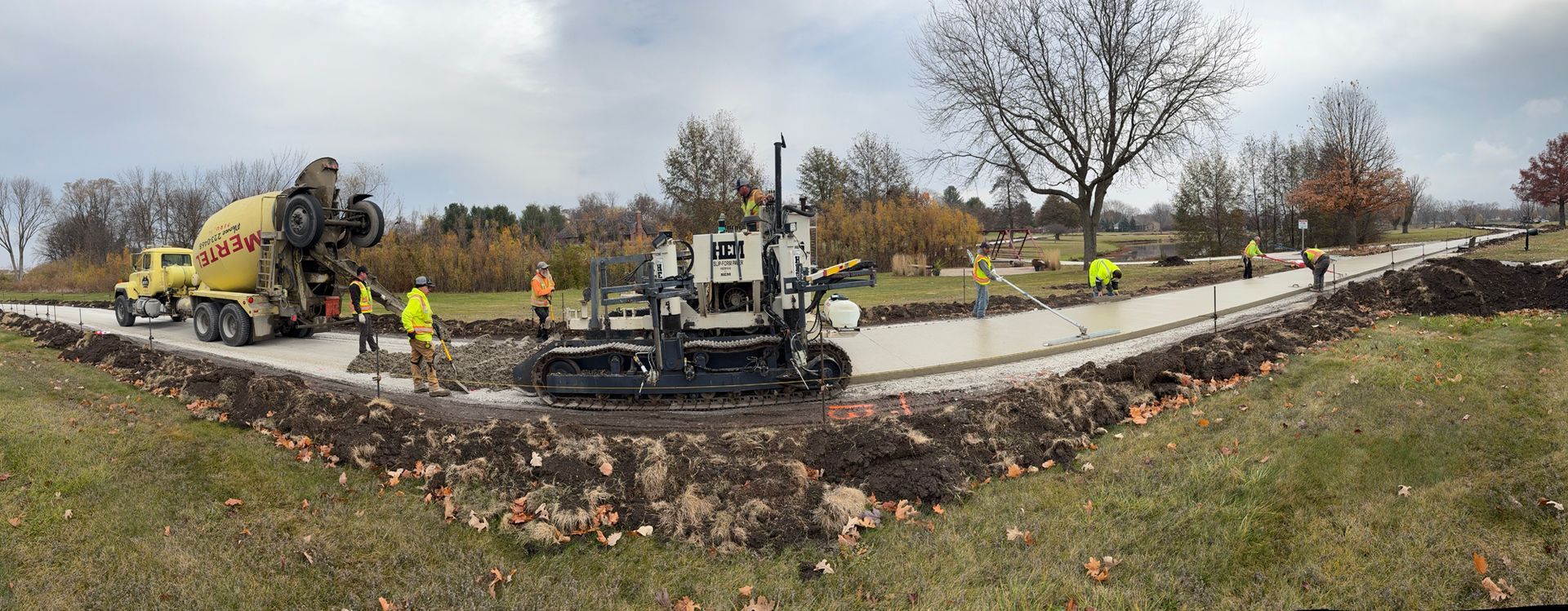Construction of a road with a cement mixer, asphalt paving machine, and workers in safety vests.