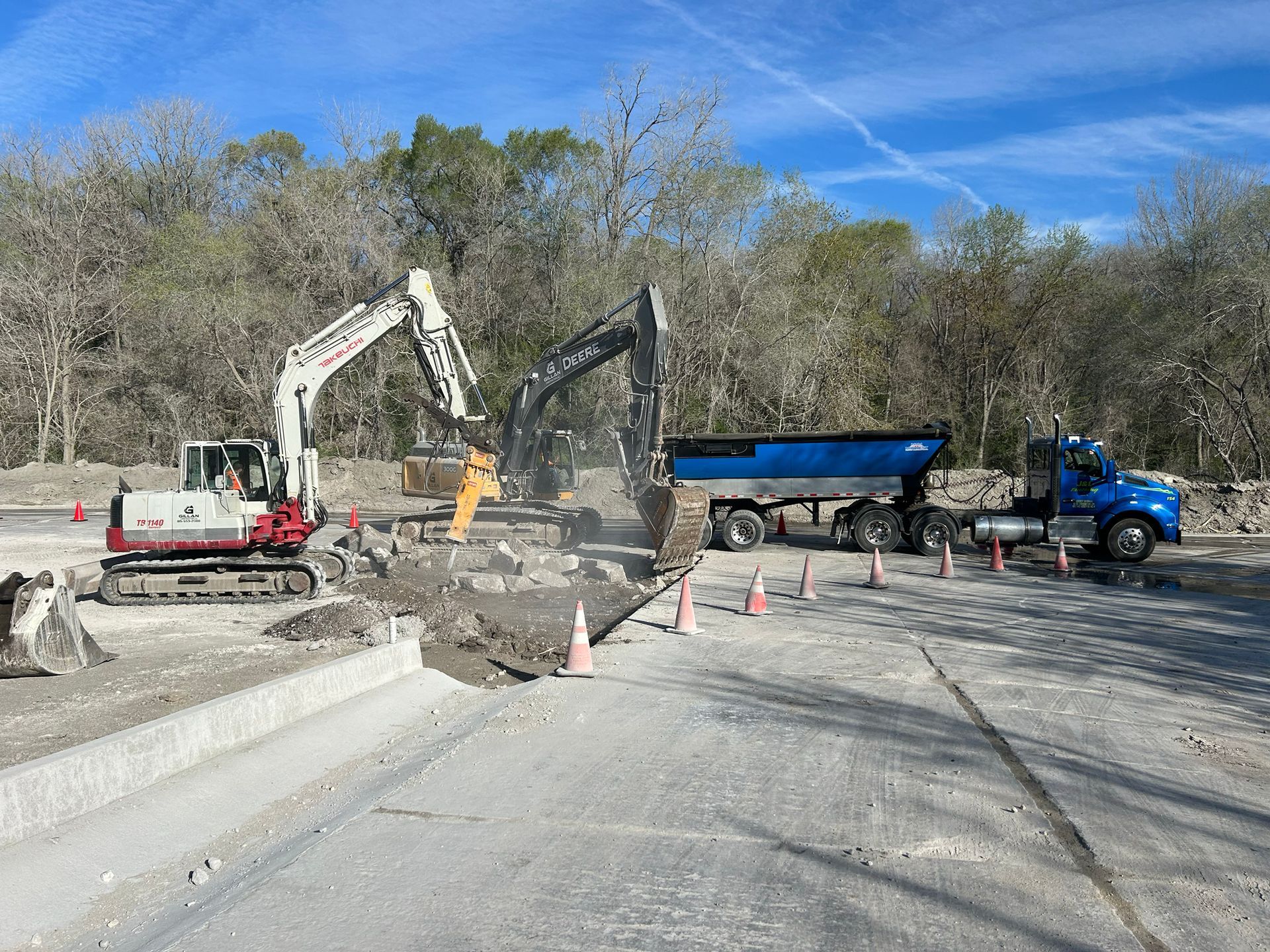 Two excavators working on road, loading truck with debris on a sunny day.