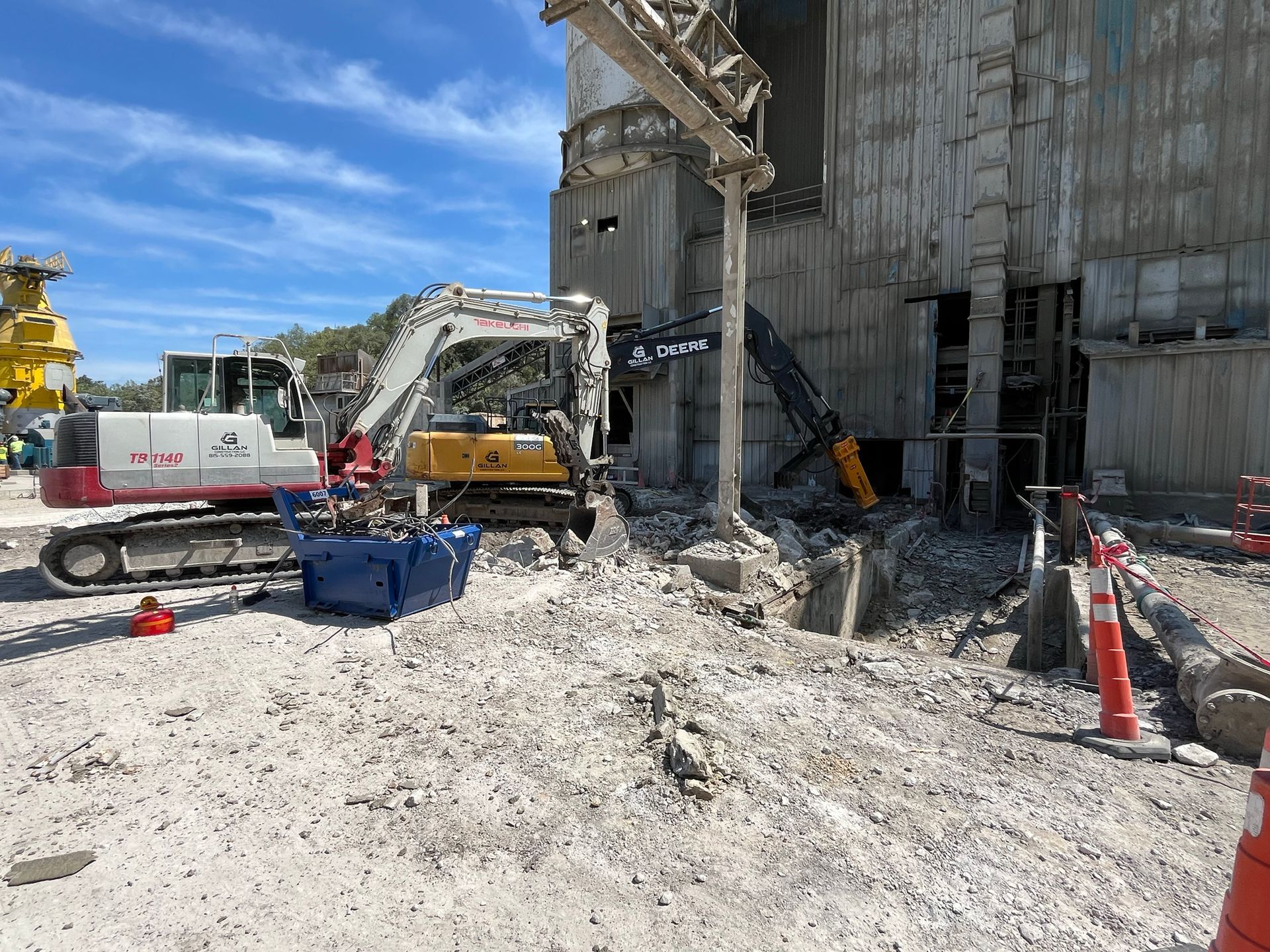 Construction site with excavators demolishing a concrete structure under a blue sky.