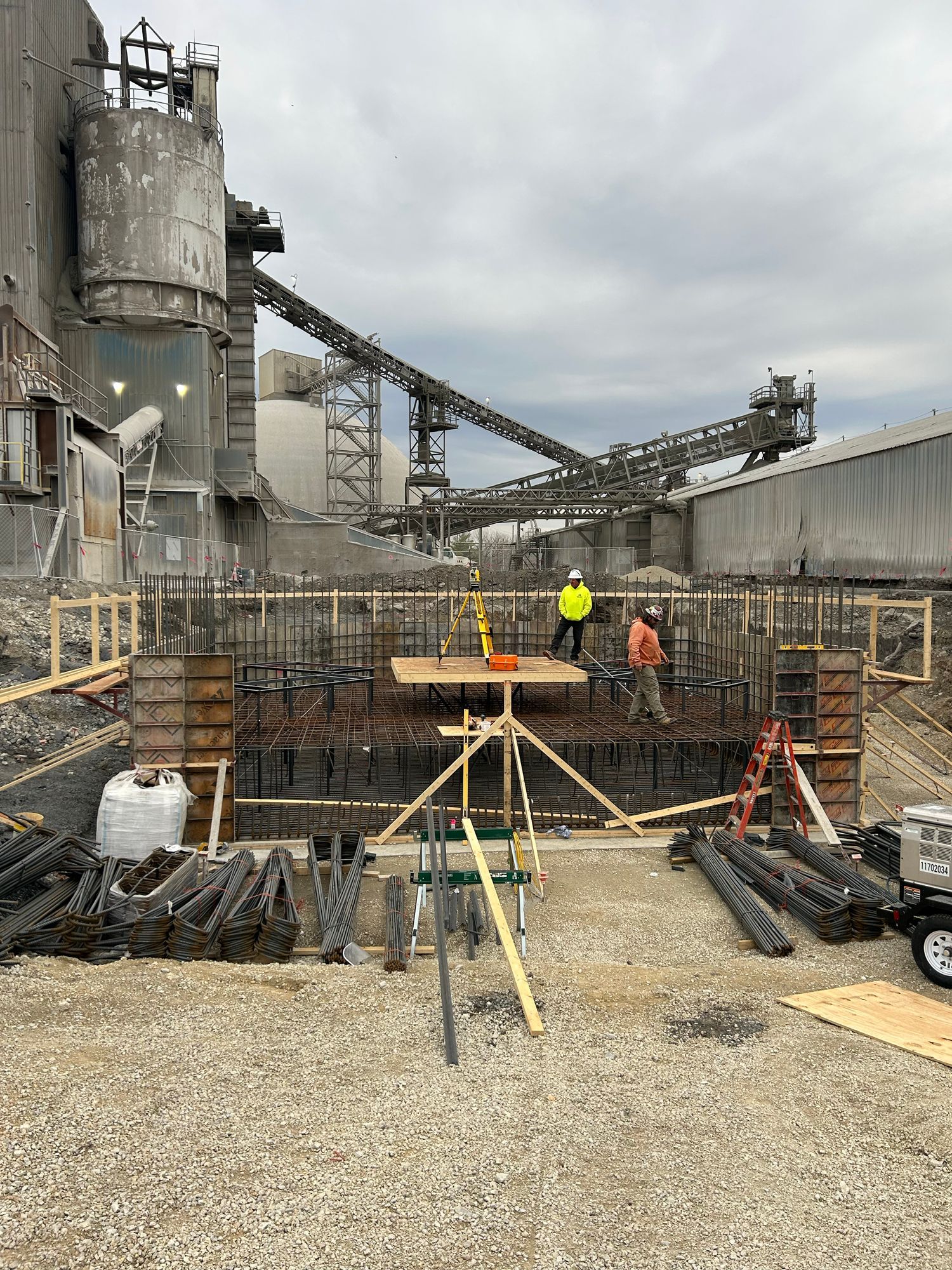 Construction site: Workers building concrete structure; industrial backdrop with conveyor belts and silos.