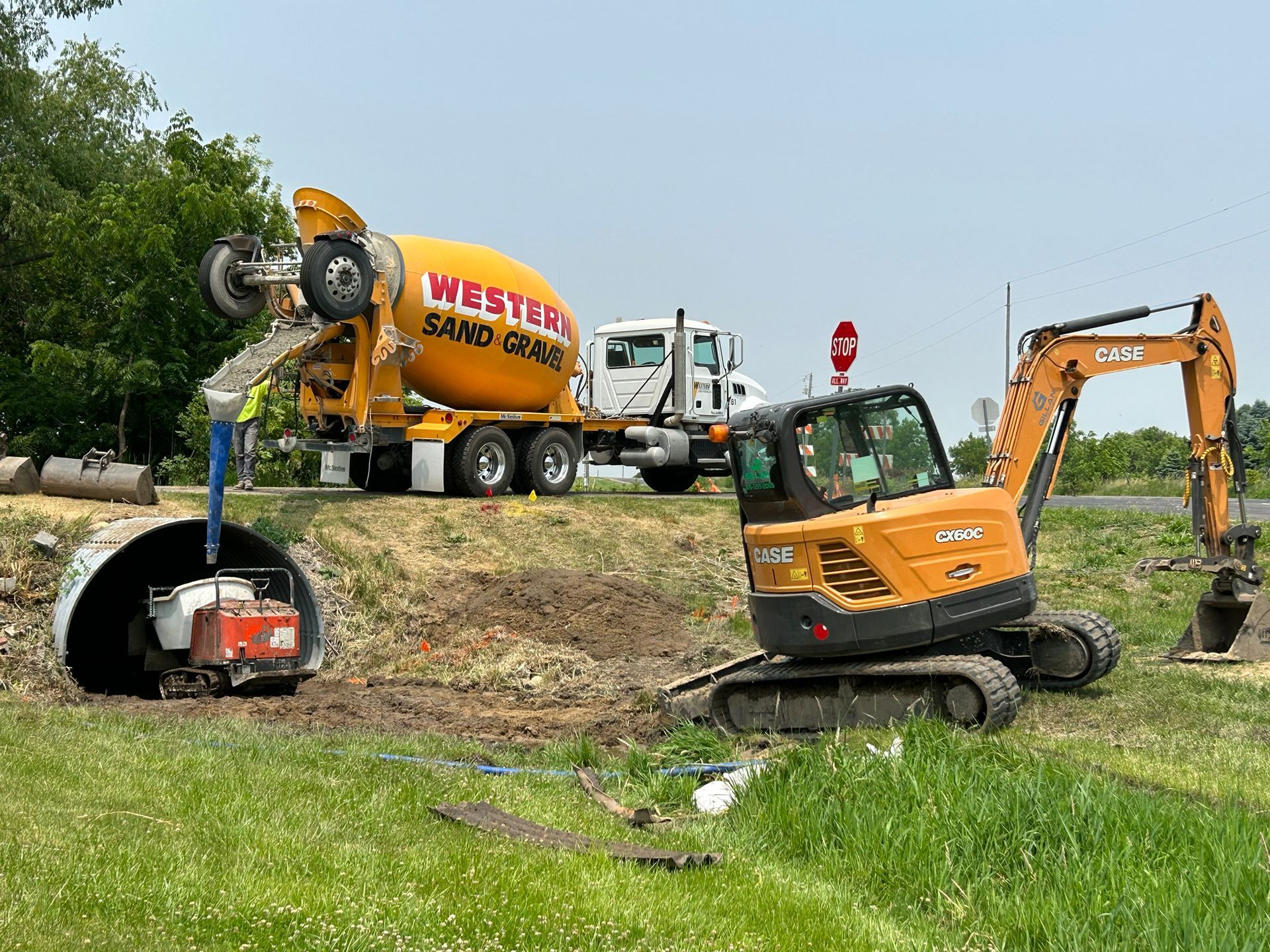 Construction site with a concrete truck pouring concrete into a culvert, an excavator, and a ditch.