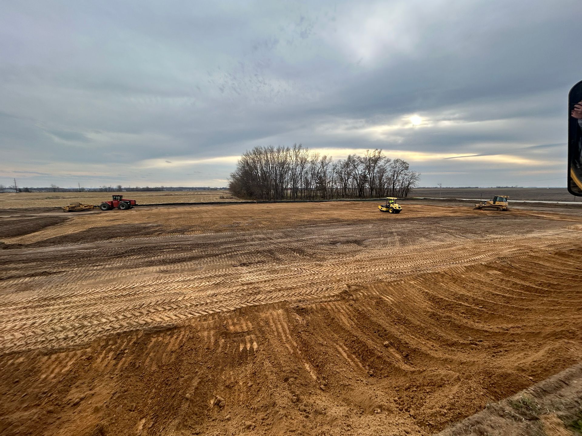 Construction site with tractors leveling earth under a cloudy sky.