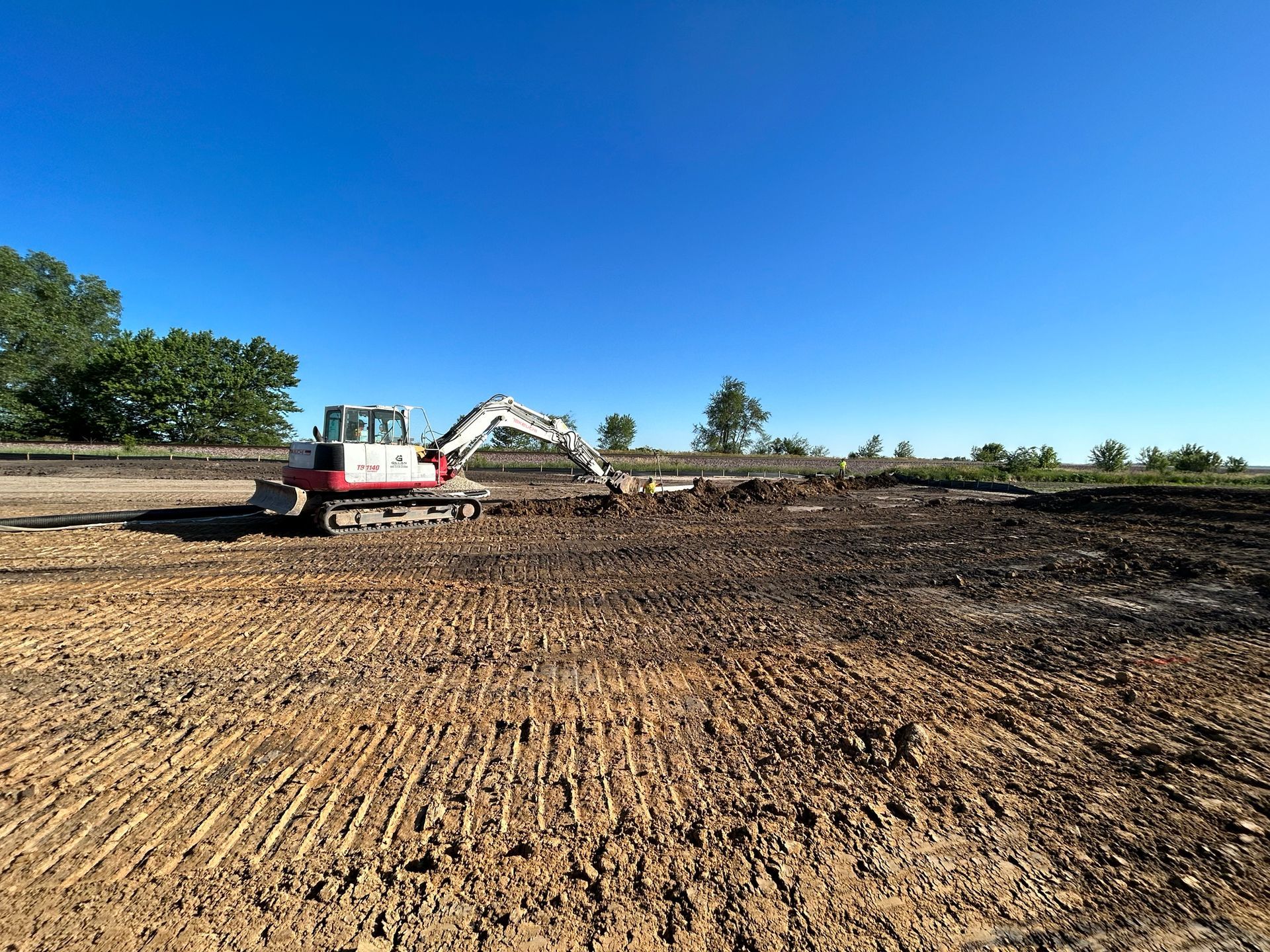 Excavator working on a brown dirt field under a clear blue sky.