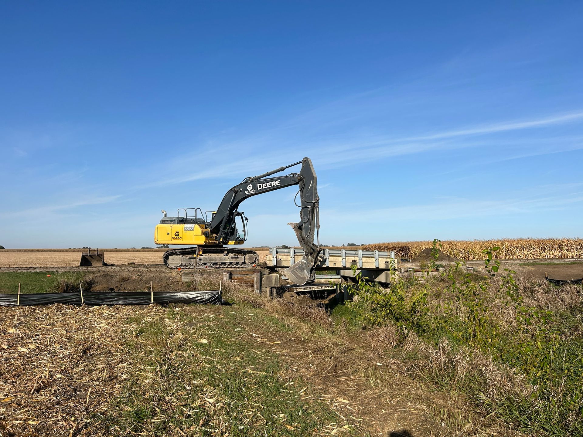 Yellow excavator operating near a small bridge in a field under a blue sky.