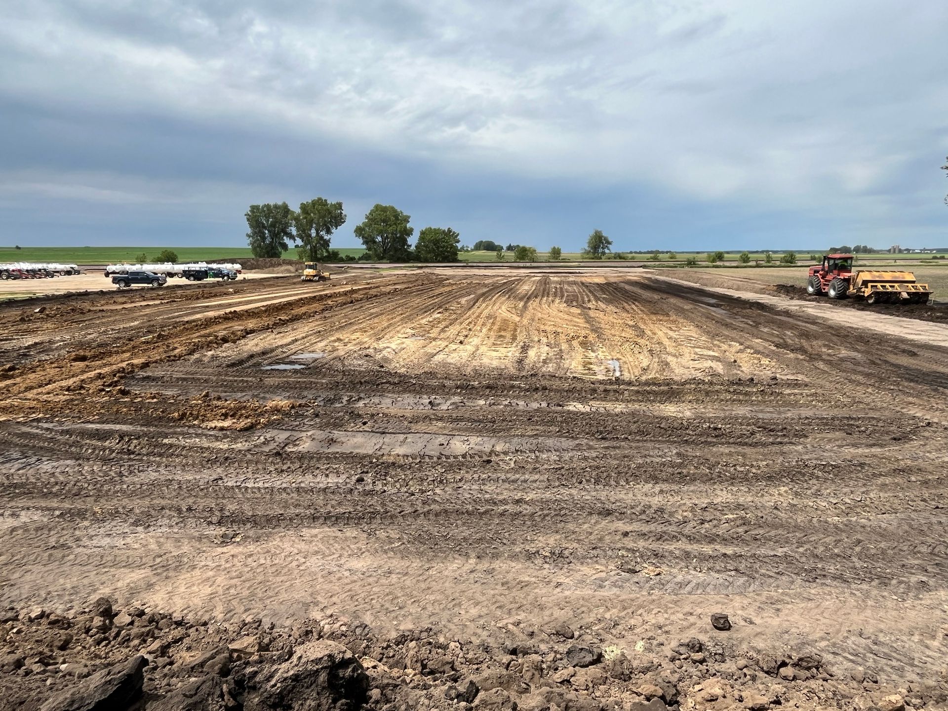 A recently plowed field under a cloudy sky. Tractor and equipment visible in the distance.