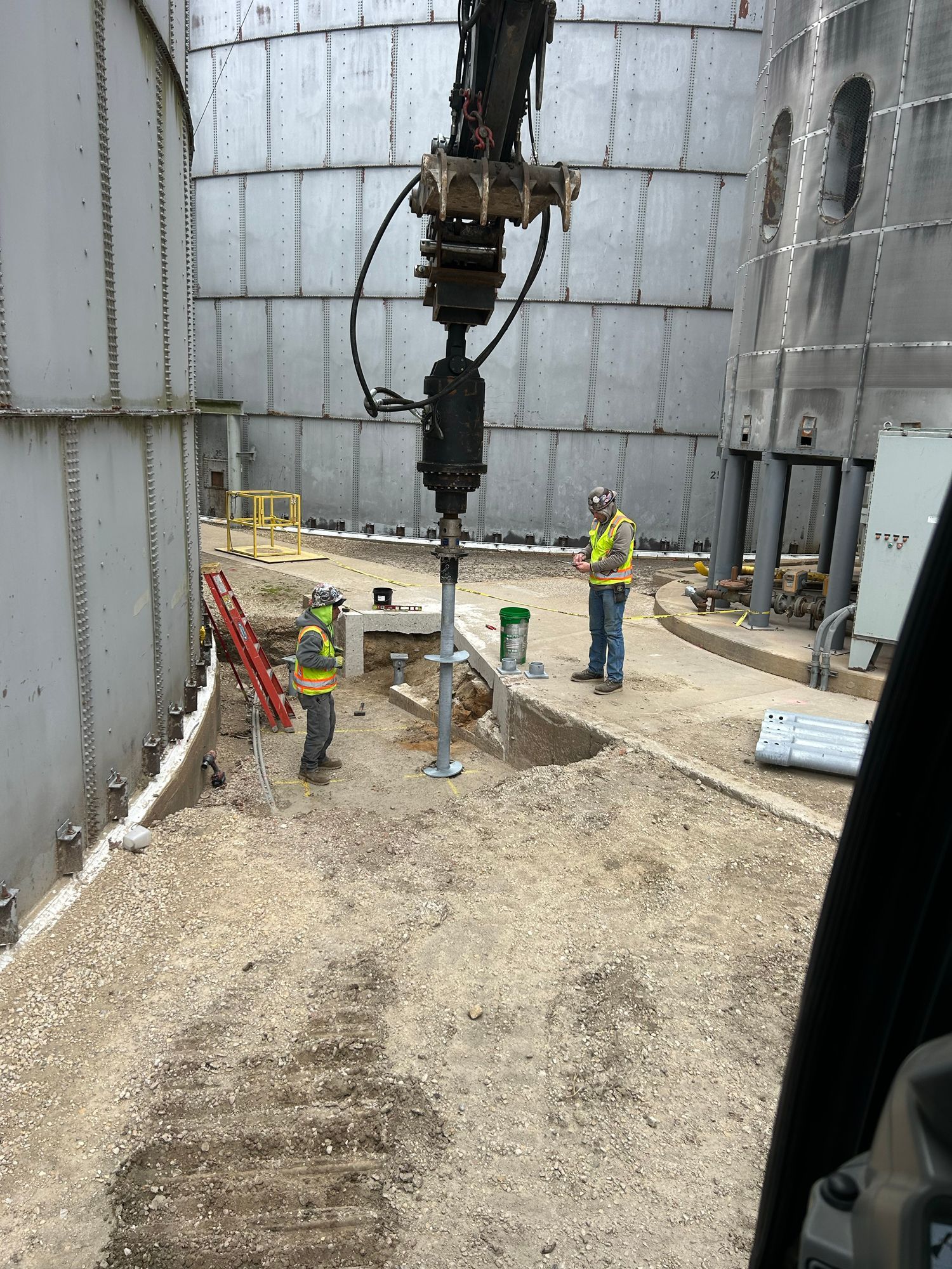 Construction workers operating equipment near large industrial tanks.