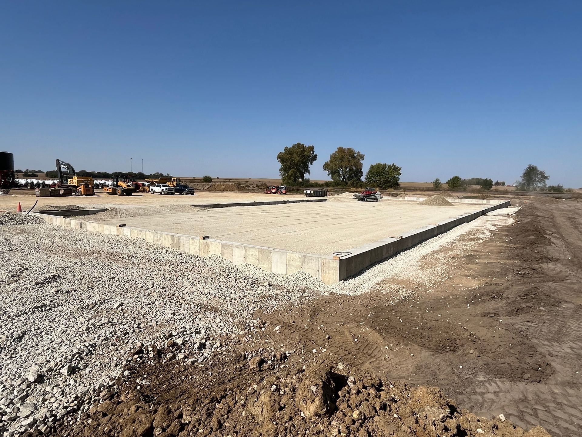 Construction site with a concrete foundation, gravel, and heavy equipment.