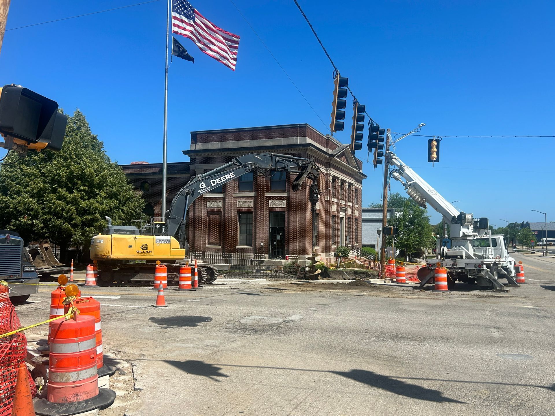 Construction site with excavator and crane near an old brick building; American flag flies above.