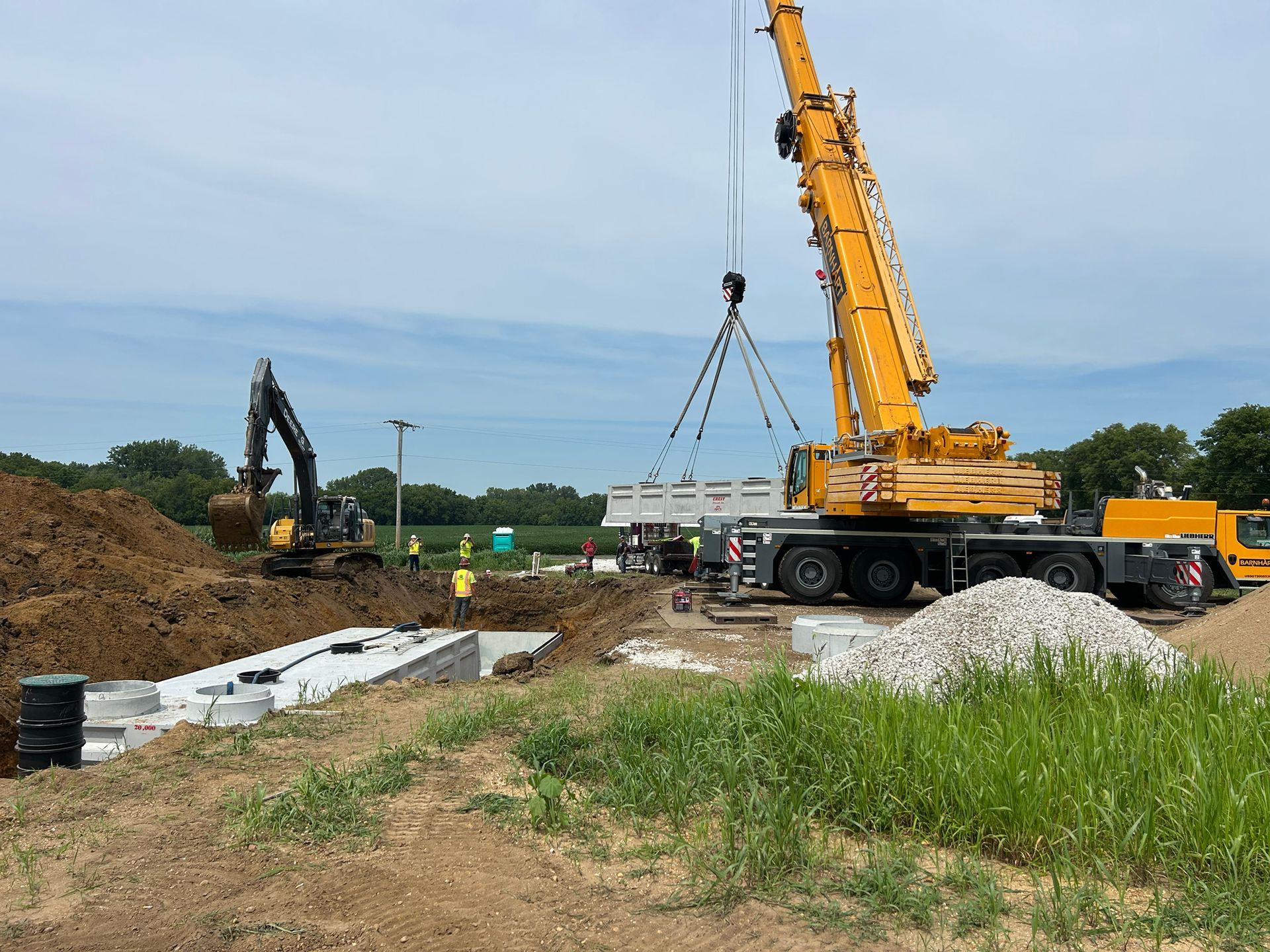 Construction site with a crane lifting a concrete slab. An excavator digs in the background.