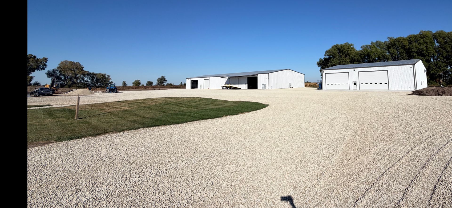 Buildings on gravel drive with green grass patch. Trees and blue sky.