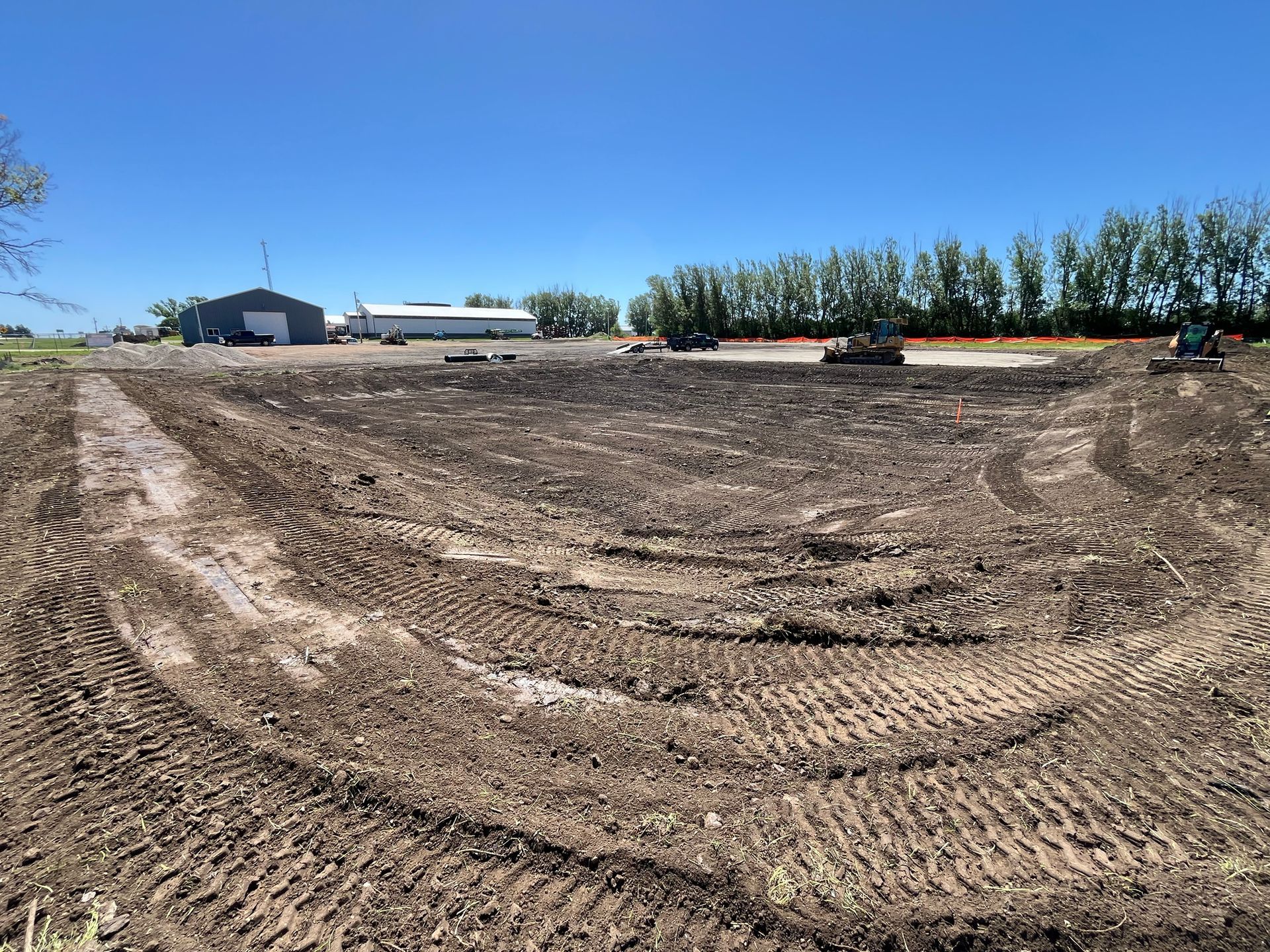 Earthmoving site; brown soil, machinery, clear blue sky, buildings in the distance.
