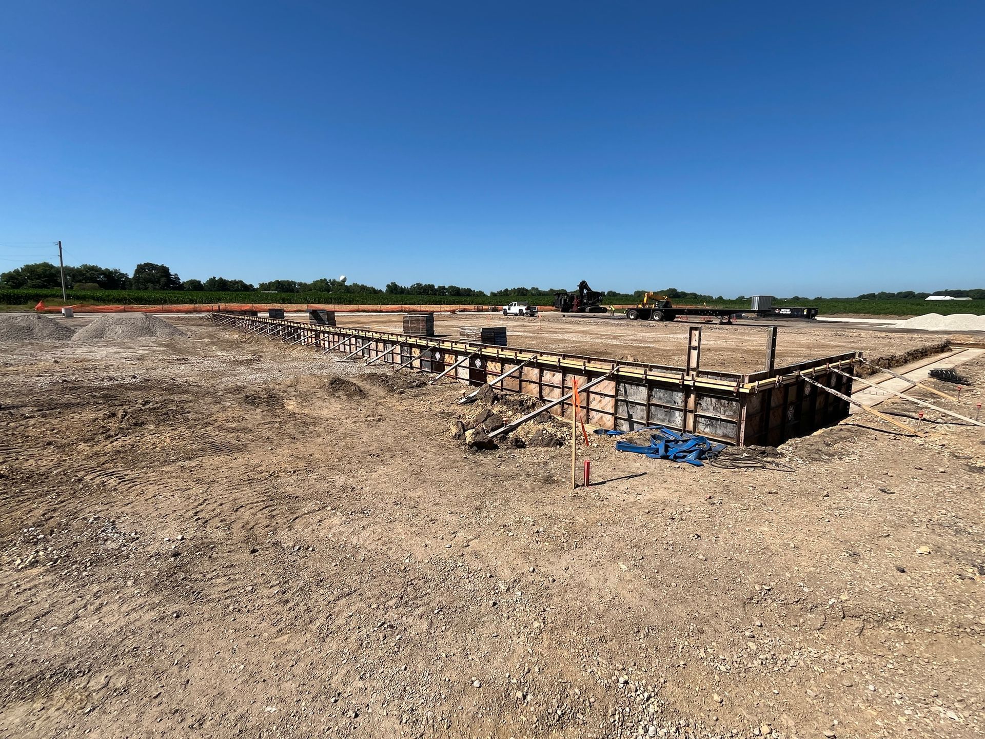 Construction site with wooden forms for foundation on a gravel-covered expanse under a blue sky.